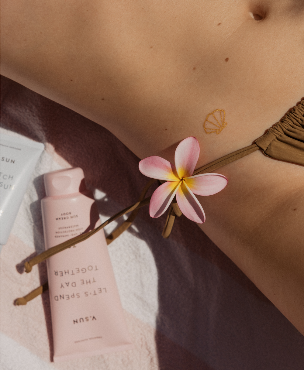 V.SUN Sonnencreme und goldenes Tattoo auf Haut mit Blume in sommerlicher Szene