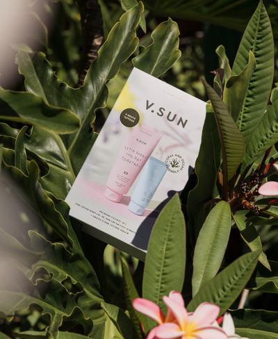 V.SUN Festival Set mit SPF-Produkten in tropischer Umgebung zwischen grünen Blättern.