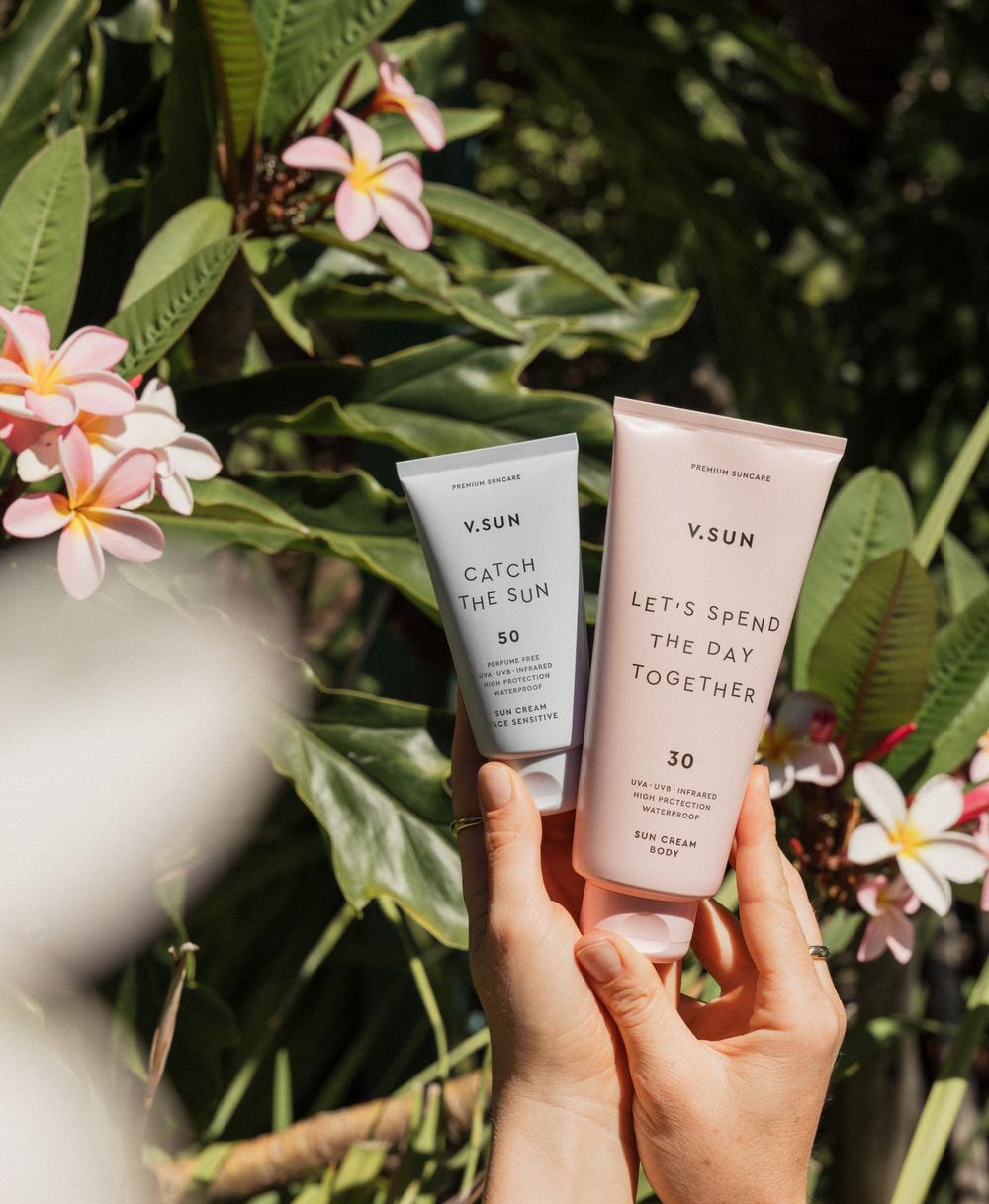V.SUN Face Cream SPF 50 und Body Cream SPF 30 in Händen vor tropischer Kulisse
